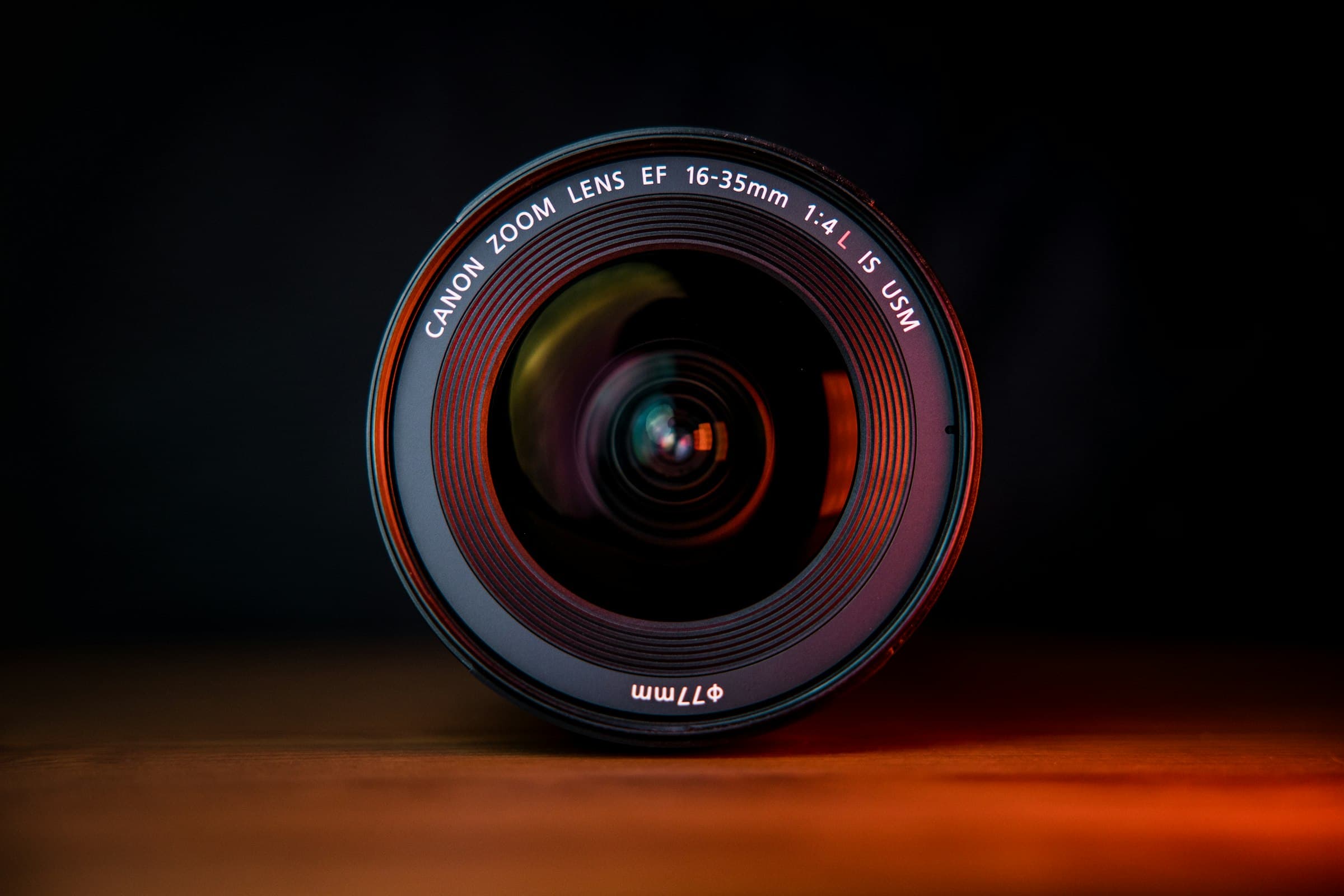 Black professional camera lens resting on a brown wooden surface